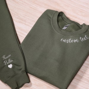 May include: A green sweatshirt and sweatpants set with white embroidery. The sweatshirt has "custom text" embroidered on the front and the sweatpants have "Kevin Bella" and a heart embroidered on the leg.