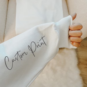 May include: White sweatshirt with the text "Custom Print" written in black on the sleeve.