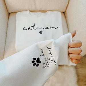 May include: White sweatshirt with the text "cat mom" and a paw print on the front. The sleeve has the text "Simply Pawsome" and a paw print.