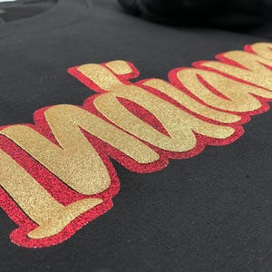May include: Black sweatshirt with the word "Indians" in gold glitter lettering outlined in red. The text is in a cursive font. The sweatshirt is made of a soft material.