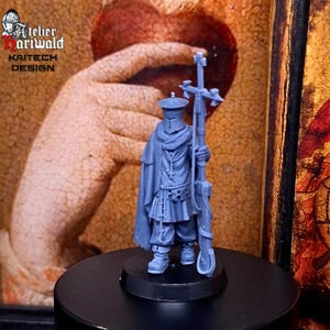 Puede incluir: Una figura en miniatura azul de un soldado medieval sosteniendo un bastón con una cruz en la parte superior. La figura lleva un sombrero, capa y túnica. La base de la figura es negra. La imagen incluye el texto "Atelier Hariwald" y "Kaitech Design".
