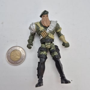 Peut inclure: Une figurine d'action militaire vêtue d'un uniforme de camouflage, d'un béret et d'un couvre-visage. La figurine a des bottes noires, une épaulette argentée et une ceinture utilitaire. Une pièce de deux dollars canadiens est à côté de la figurine.