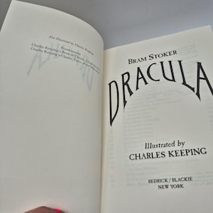 Może przedstawiać: Otwarta książka w twardej oprawie zatytułowana Dracula autorstwa Brama Stokera, z ilustracjami Charlesa Keepinga, wydana przez Bedrick/Blackie New York. Lewa strona wymienia inne prace ilustratora, a prawa strona zawiera tytuł i informacje.