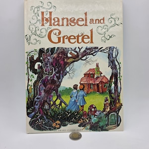 Peut inclure: Un livre relié intitulé Hansel and Gretel avec une couverture crème présentant une illustration colorée de deux enfants dans une forêt près d'une maison, avec une pièce d'argent placée au centre en bas pour l'échelle sur la couverture.