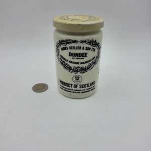 May include: A cream-colored ceramic jar with a matching lid, featuring black printed text that reads James Keiller & Son Ltd. Dundee Seville Orange Marmalade, 12 fluid oz., and Product of Scotland, accompanied by a small circular coin.