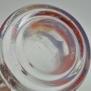 May include: Clear glass bottle base with a circular design. The base has a red, yellow, and blue painted rim. The bottom of the bottle has a small square logo and the number "42U" etched into the glass.