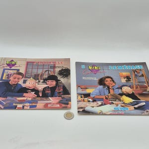 May include: Two vintage French children's books, "Bibi et Geneviève", are displayed. The covers feature illustrations of children and puppets. The book on the left is titled "J'accueille..." and the one on the right is "Le Ménage". A coin is in the foreground.