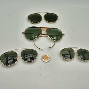 May include: An assortment of vintage sunglasses and clip-on lenses with gold-colored frames and green lenses. The sunglasses are in various styles, including aviator and clip-on designs. A Canadian coin is also present.