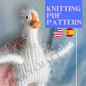 Op de afbeelding: Gebreid wit amigurumi speelgoed in de vorm van een gans met oranje voeten. Het speelgoed wordt in een hand gehouden. De afbeelding bevat de tekst "Knitting PDF Pattern" en vlaggen voor de Verenigde Staten en Spanje.
