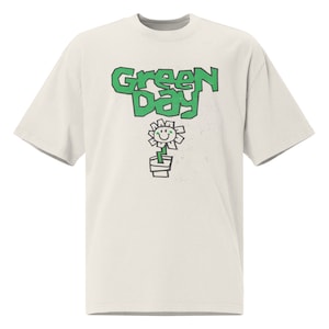 Może przedstawiać: Biała koszulka z zielonym logo "Green Day" i zielonym rysunkowym kwiatem z uśmiechem.