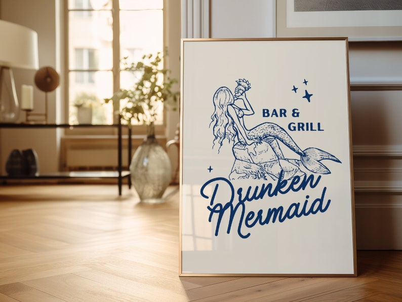 May include: A white sign with a gold frame featuring a blue illustration of a mermaid holding a drink. The text on the sign reads "Bar & Grill Drunken Mermaid" with stars on either side of the text.