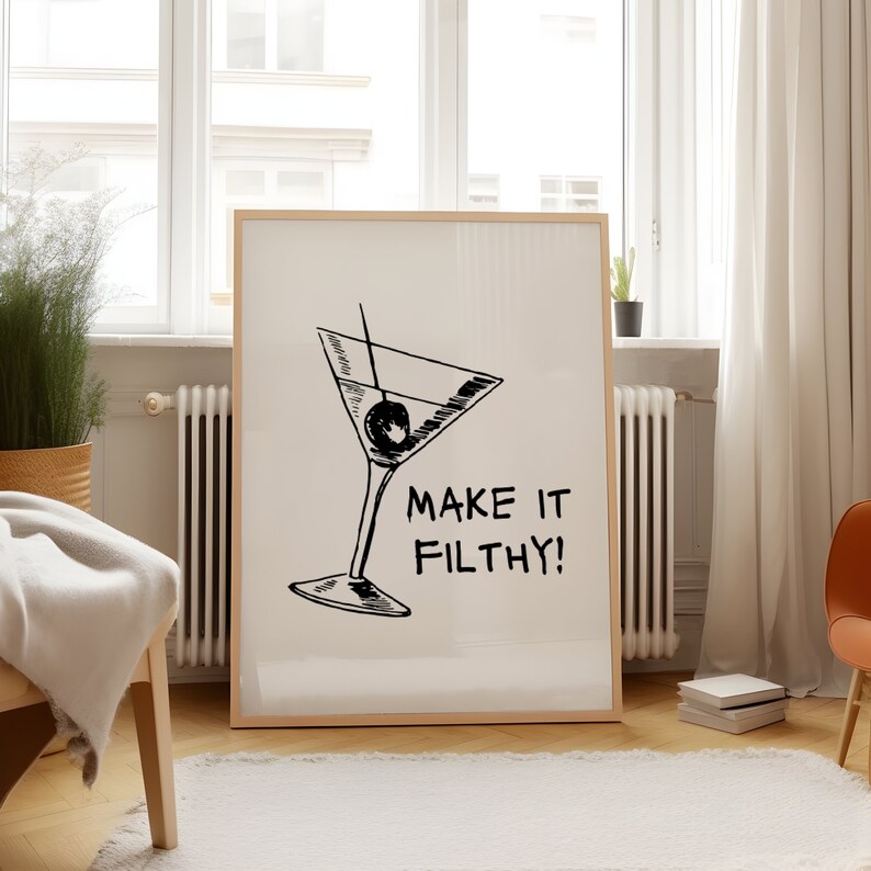 May include: A black and white illustration of a martini glass with an olive, with the text "Make it Filthy!" printed below the glass. The illustration is on a white background and framed in a light wood frame.