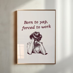May include: A framed print featuring a black and white illustration of a woman with her head in her hands. The text "Born to yap, forced to work" is printed in maroon above the illustration.
