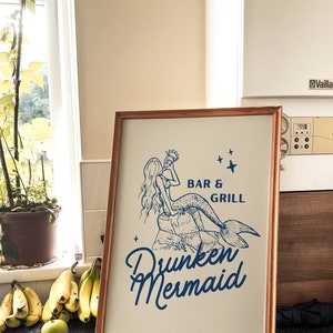 May include: A framed print with a blue illustration of a mermaid holding a seashell. The text "Bar & Grill" and "Drunken Mermaid" is written in blue below the illustration.