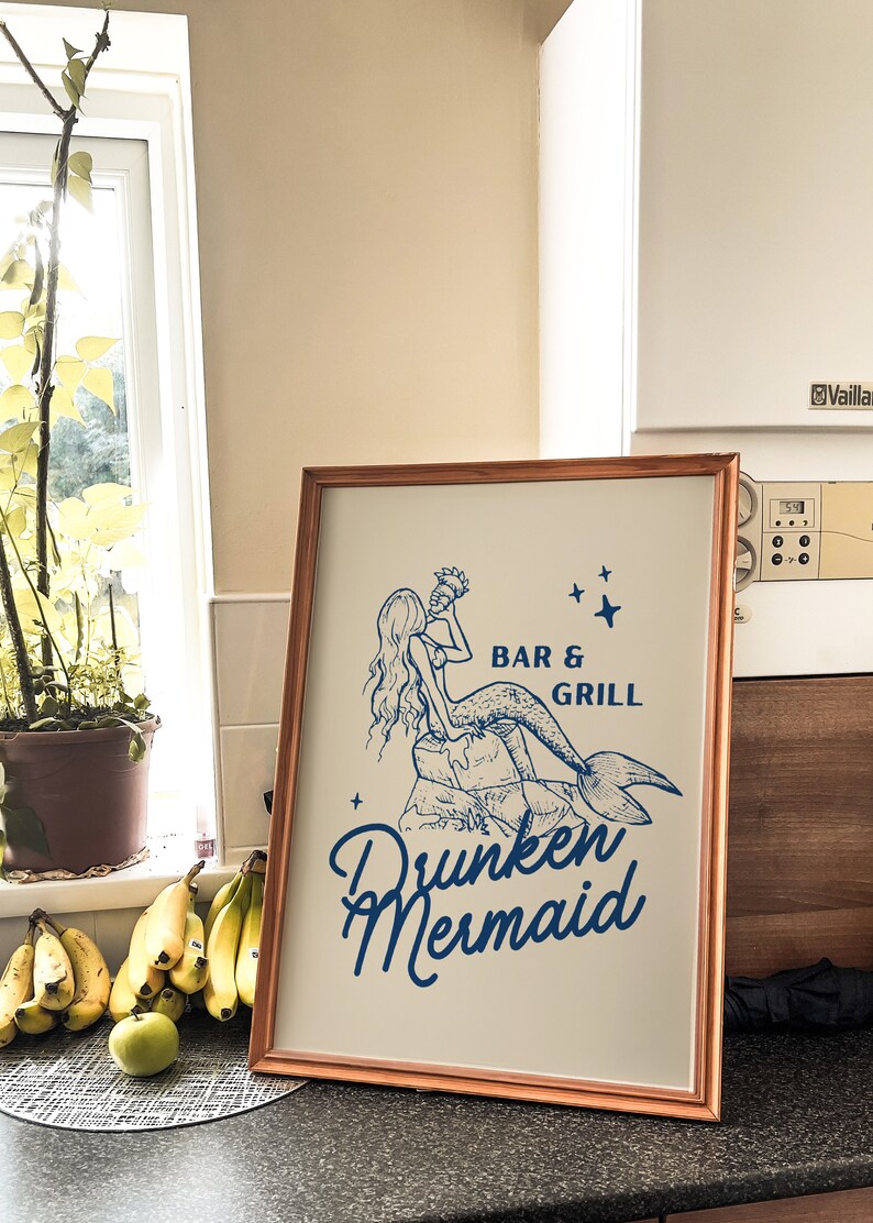 May include: A framed print with a blue illustration of a mermaid holding a seashell. The text "Bar & Grill" and "Drunken Mermaid" is written in blue below the illustration.