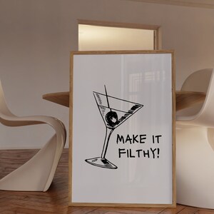 May include: A white framed poster with a black and white illustration of a martini glass with an olive. The text "MAKE IT FILTHY!" is below the illustration.