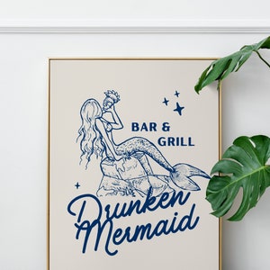 May include: A framed illustration of a mermaid drinking from a seashell with the text "Drunken Mermaid Bar & Grill" in blue lettering on a beige background.