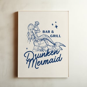 May include: A white framed print with a blue illustration of a mermaid holding a seashell. The text "BAR & GRILL" and "Drunken Mermaid" is printed below the illustration.