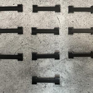 May include: Ten black plastic clips, each with two prongs, arranged in three rows on a gray textured surface.