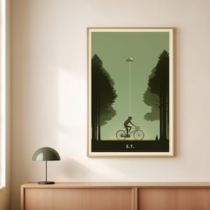 May include: A framed poster featuring a silhouette of a person riding a bicycle towards a UFO, with the text "E.T." at the bottom. The artwork is set in a forest with tall trees on either side, and the color palette is primarily green and brown.