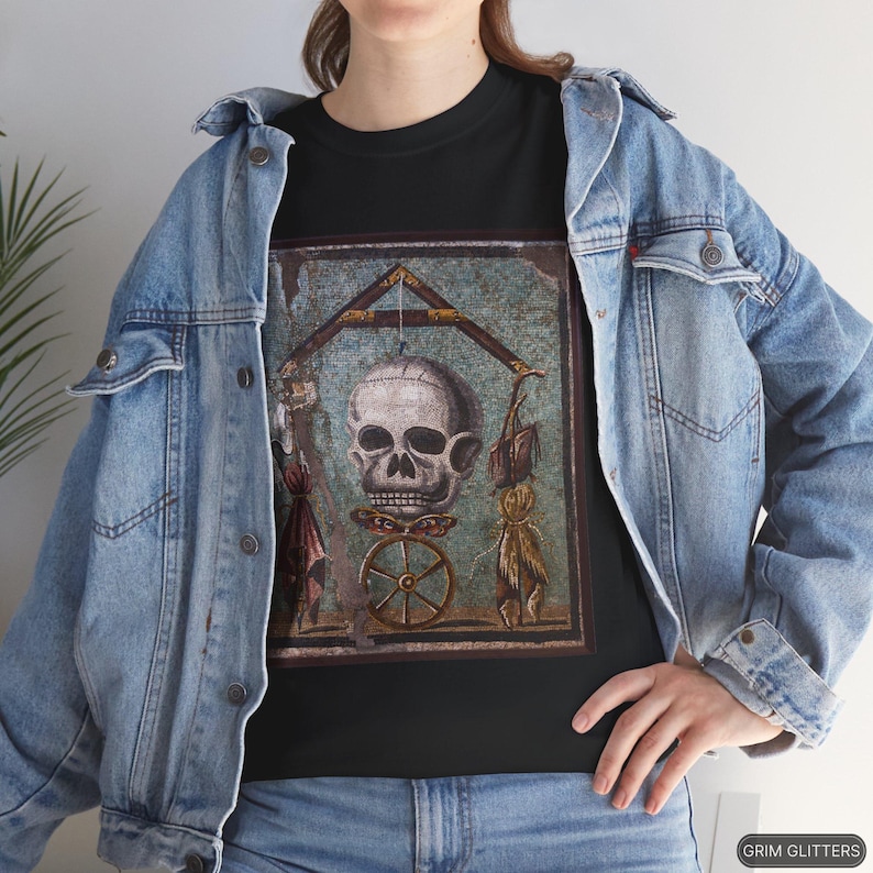 May include: A black t-shirt with a vintage-style image of a skull with a wheel and other symbols. The image is surrounded by a blue and green mosaic-like frame.