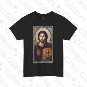 May include: Black t-shirt featuring a religious icon of Jesus Christ. The image depicts Jesus with a halo, holding a book, and is framed with a blue border. The shirt is a classic crew neck style.