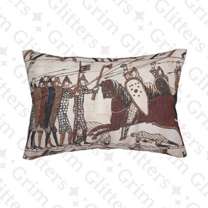 Puede incluir: Una almohada beige con un diseño de tapiz marrón y blanco que representa una escena del Tapiz de Bayeux. La escena muestra a un grupo de hombres armados a pie, frente a un caballero montado con un escudo y una espada.