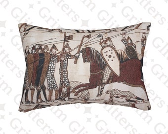 May include: A beige pillow with a brown and white tapestry design depicting a scene from the Bayeux Tapestry. The scene shows a group of armed men on foot, facing a mounted knight with a shield and a sword.