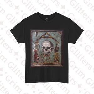 May include: Black t-shirt with a graphic print of a skull in a mosaic frame. The skull is suspended from a wooden structure with a wheel below it.