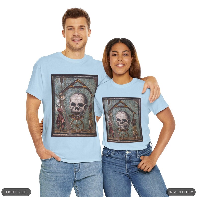 May include: Two people wearing light blue t-shirts with a vintage mosaic image of a skull on a wheel. The mosaic is framed in black. The image is from the Grim Glitters collection.