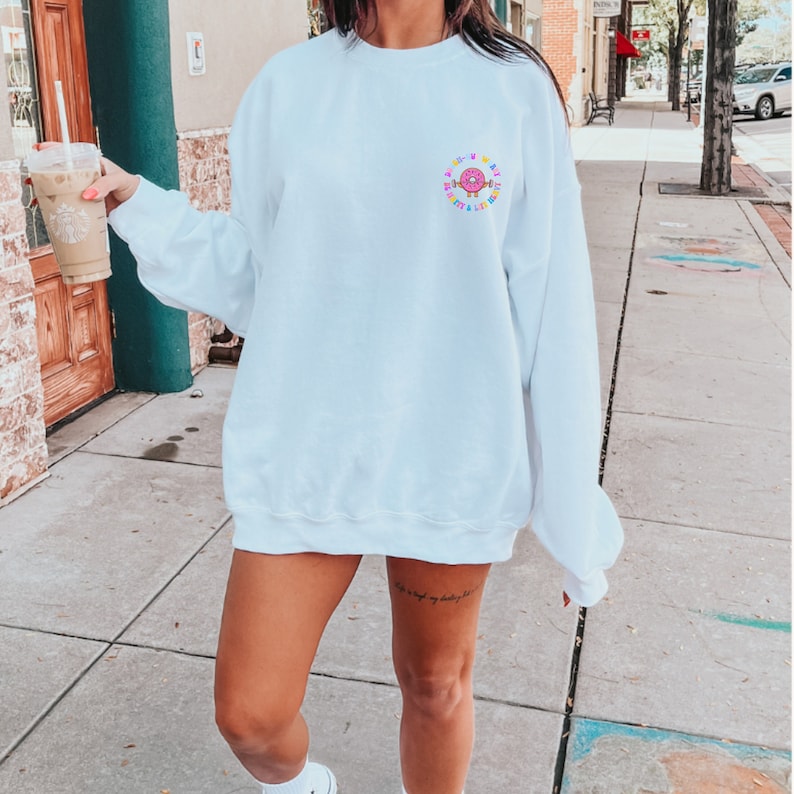 May include: White sweatshirt with a colorful donut graphic and the text "A little me, a little messy".
