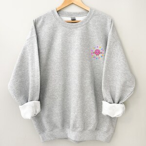 May include: A gray sweatshirt with a pink donut graphic on the left chest. The donut is surrounded by colorful sprinkles and the text "Donut Worry Be Happy".