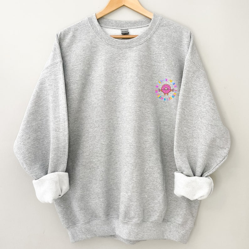 May include: A gray sweatshirt with a pink donut graphic on the left chest. The donut is surrounded by colorful sprinkles and the text "Donut Worry Be Happy".