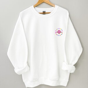 May include: White sweatshirt with a colorful donut graphic and the text "Don't worry, be happy & lift heavy".
