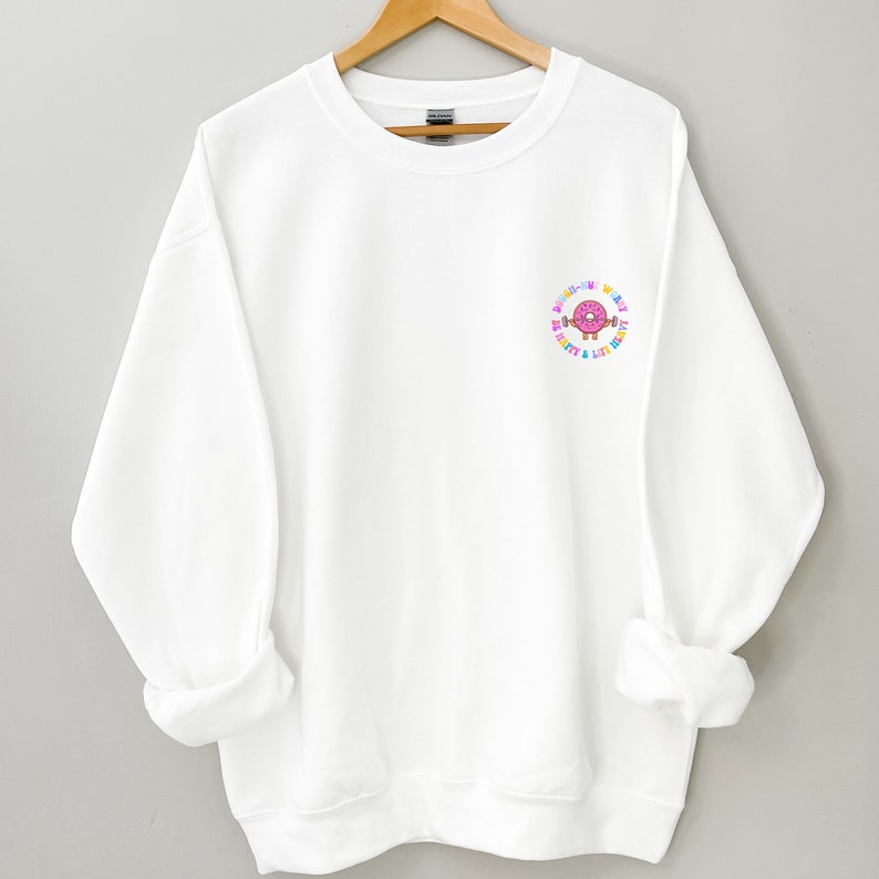 May include: White sweatshirt with a colorful donut graphic and the text "Don't worry, be happy & lift heavy".