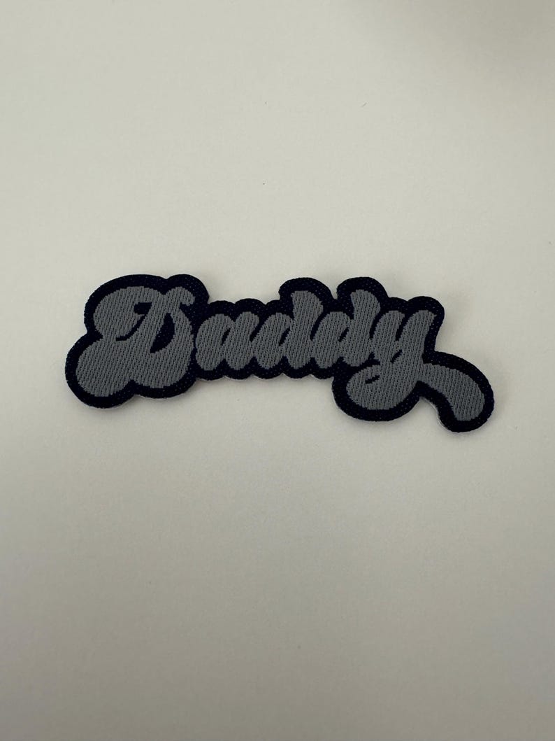 May include: A gray embroidered patch with the word "Dudley" in a stylized font.