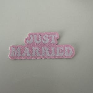 May include: Pink fabric patch with white text that reads "JUST MARRIED" in a retro font.