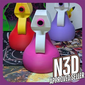 May include: Three 3D printed figurines, each with a different color: red, purple, and pink. The figurines have a unique design with a circular opening on the top and a handle on the side. The figurines are sitting on a black surface with a colorful design.