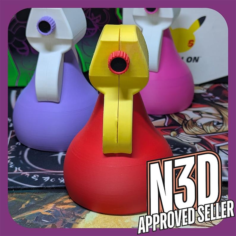 May include: Three 3D printed spray bottles in different colors: purple, red, and pink. The bottles have a yellow nozzle and a red button on the top. The bottles are sitting on a black and white surface with the text "N3D APPROVED SELLER" in the foreground.