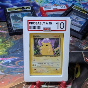 May include: A Pikachu trading card encased in a white protective slab with a red and white label reading PROBABLY A 10 and the number 10. The card features a yellow character, 40 HP, and attacks named Gnaw and Thunder Jolt with text details.