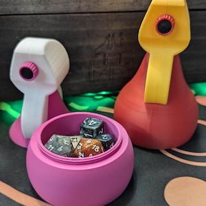 May include: Two 3D printed dice towers, one white and one red, with a pink dice tower with a lid open and dice inside. The dice are various colors and have different numbers on them.