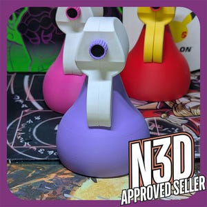May include: Three 3D printed spray bottles in different colors: pink, purple, and red. The bottles have a white nozzle and a white handle. The bottles are sitting on a black and white surface.