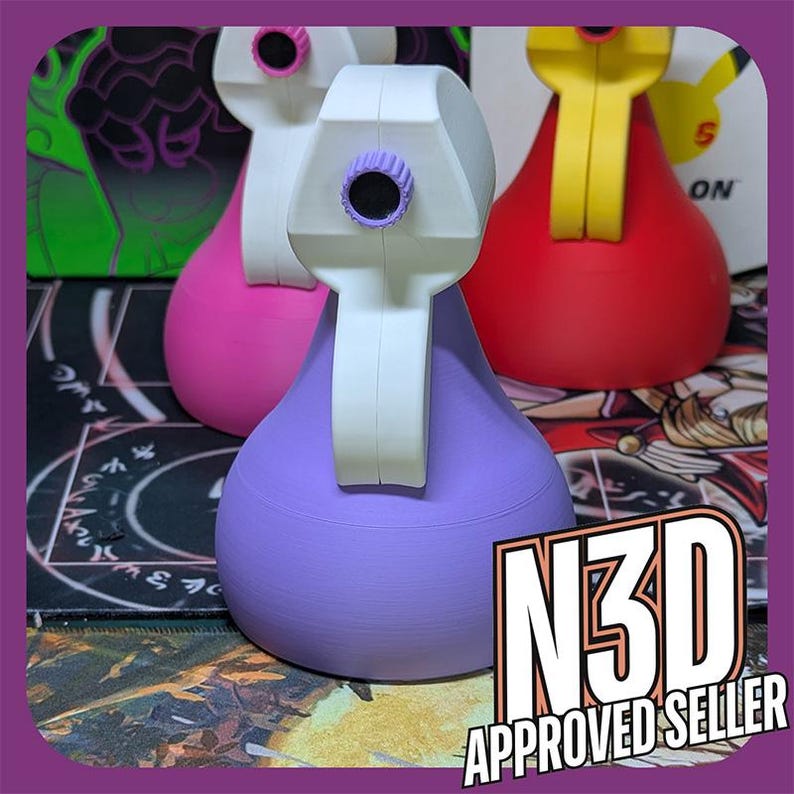 May include: Three 3D printed spray bottles in different colors: pink, purple, and red. The bottles have a white nozzle and a white handle. The bottles are sitting on a black and white surface.