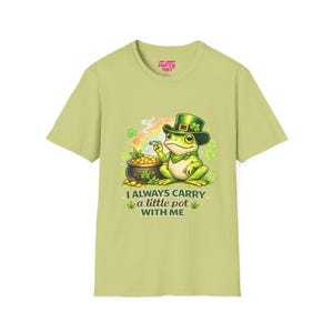 Peut inclure: T-shirt vert clair avec une grenouille de dessin animé portant un chapeau vert et fumant. La grenouille est à côté d'un pot d'or et d'un arc-en-ciel. Le texte sur le t-shirt se lit "I ALWAYS CARRY a little pot WITH ME."