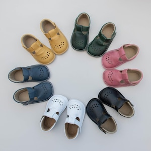 Peut inclure: Une collection de chaussures pour bébés disposées en cercle. Les chaussures sont de différentes couleurs : jaune, vert, rose, bleu, blanc et noir. Chaque chaussure a une bride en T et un bout perforé.