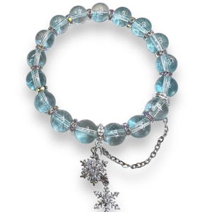 May include: A light blue glass bead bracelet with a silver snowflake charm. The bracelet has a delicate chain with a smaller snowflake charm.