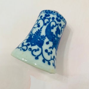 May include: A white and blue ceramic object with a flared shape. The object is decorated with a blue floral and bird design. The design is intricate and detailed, with a traditional aesthetic.