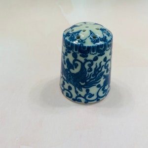 May include: A white ceramic salt shaker with a blue and white floral design featuring a phoenix. The shaker has a lid with multiple holes for dispensing salt.