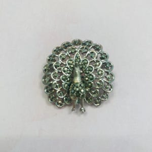 May include: A silver peacock brooch with a detailed design of a peacock with its tail feathers spread out. The peacock is made of marcasite stones.