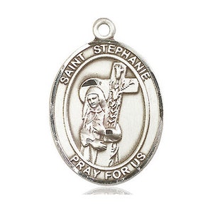 May include: Silver oval-shaped pendant featuring a depiction of Saint Stephanie holding a cross and a palm branch. The pendant reads "Saint Stephanie Pray For Us".
